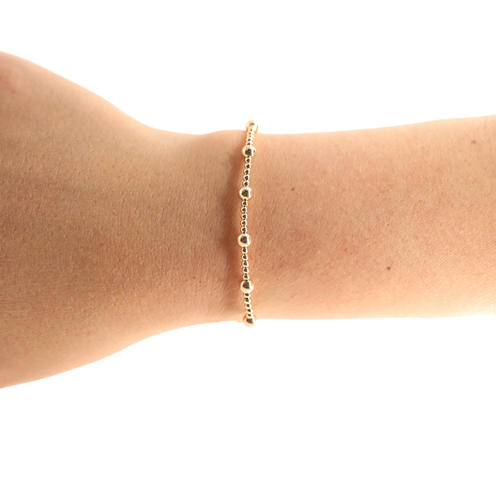 Gold bracelet on a person's wrist against a white background