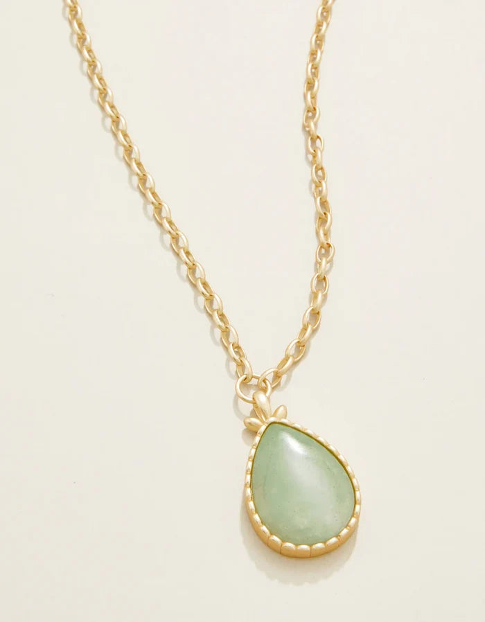 Gold necklace with a green teardrop pendant on a light beige background