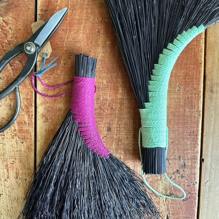 Two brooms with colorful handles and a pair of scissors on a wooden surface