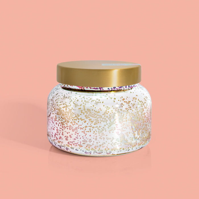 An oversized jar candle with a white and gold iridescent finish and a gold lid on a pink background.