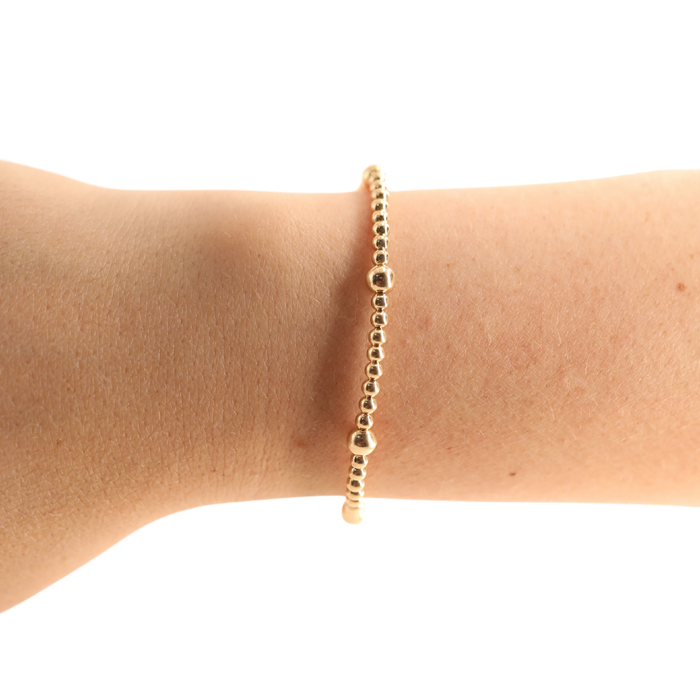 Gold bracelet on a person's wrist against a white background