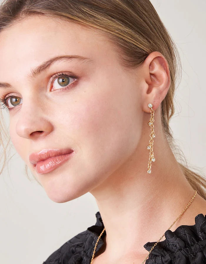 Close-up of a woman wearing gold earrings and a necklace against a neutral background