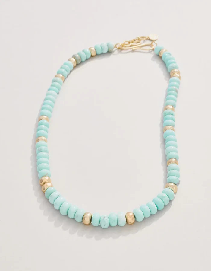 Turquoise beaded necklace with gold accents on a light gray background