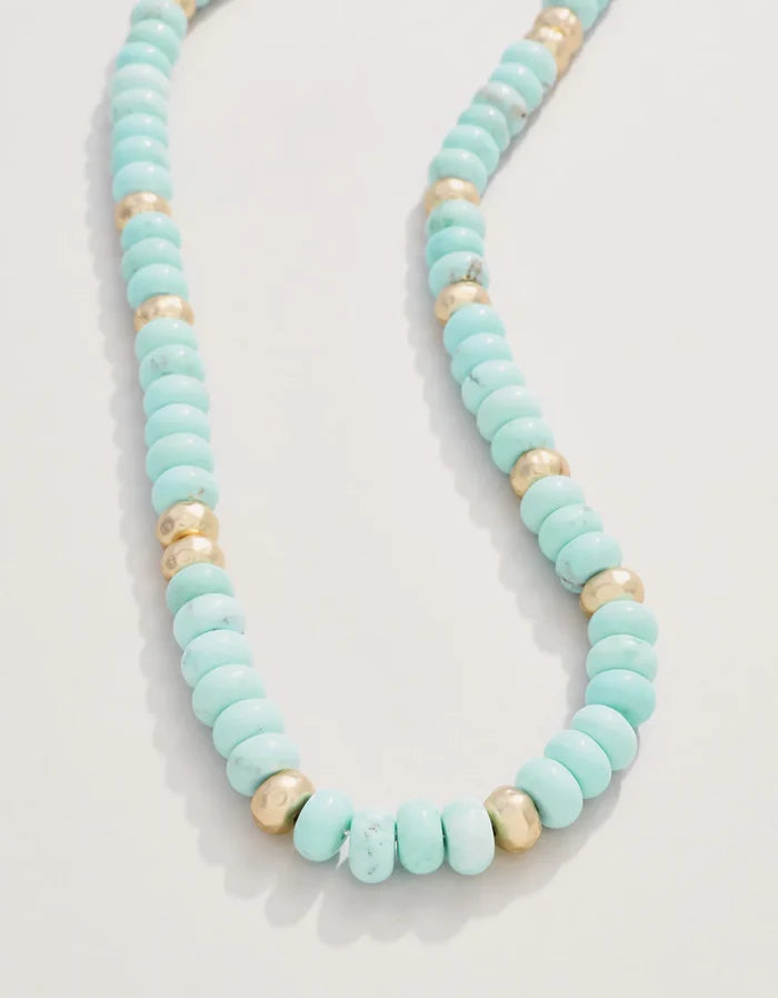 Turquoise beaded necklace with gold accents on a light gray background