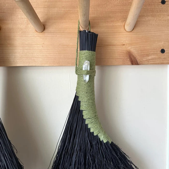Green broom with black bristles leaning against a wooden surface.