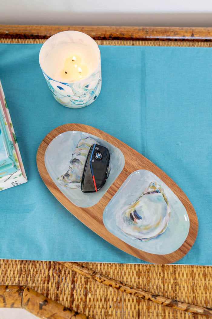 Oval wooden serving tray with oyster pattern atop a wicker table