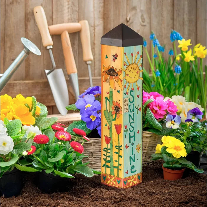 Decorative garden post with sun and flower design in a garden setting